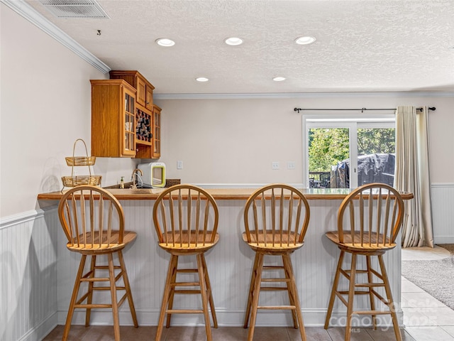 bar featuring visible vents, crown molding, a wainscoted wall, wet bar, and a textured ceiling