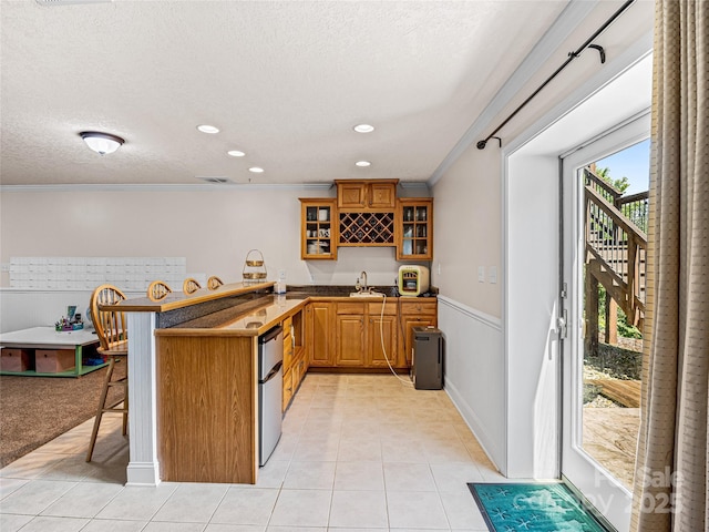 kitchen featuring a breakfast bar area, brown cabinets, a peninsula, light tile patterned flooring, and a sink