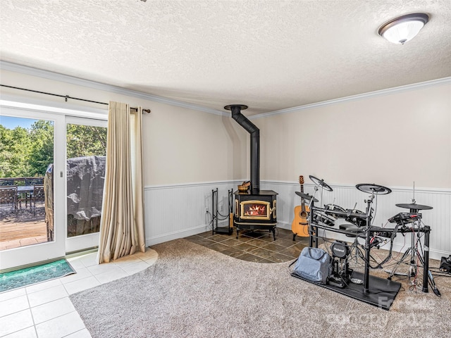 interior space with tile patterned flooring, a textured ceiling, a wood stove, and wainscoting