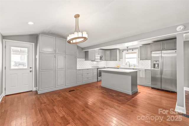 kitchen featuring gray cabinets, a sink, hardwood / wood-style floors, appliances with stainless steel finishes, and vaulted ceiling