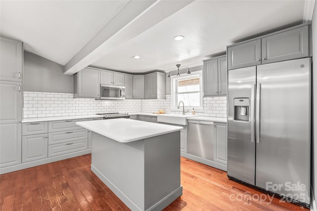 kitchen with gray cabinetry, tasteful backsplash, stainless steel appliances, light wood-style floors, and light countertops