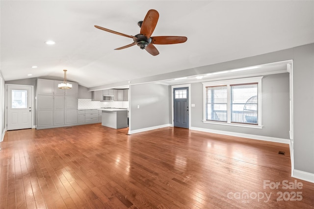 unfurnished living room with light wood-type flooring, baseboards, ceiling fan with notable chandelier, and vaulted ceiling