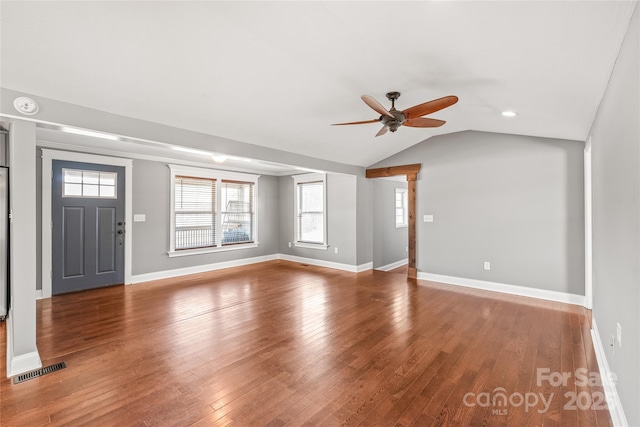 interior space with a ceiling fan, visible vents, baseboards, vaulted ceiling, and wood-type flooring