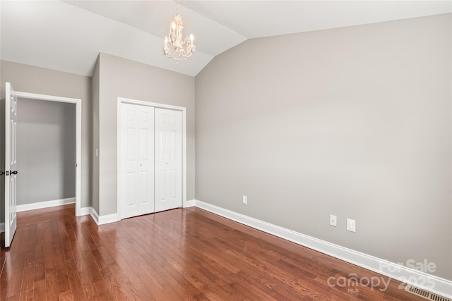 unfurnished bedroom featuring wood finished floors, a closet, baseboards, an inviting chandelier, and lofted ceiling