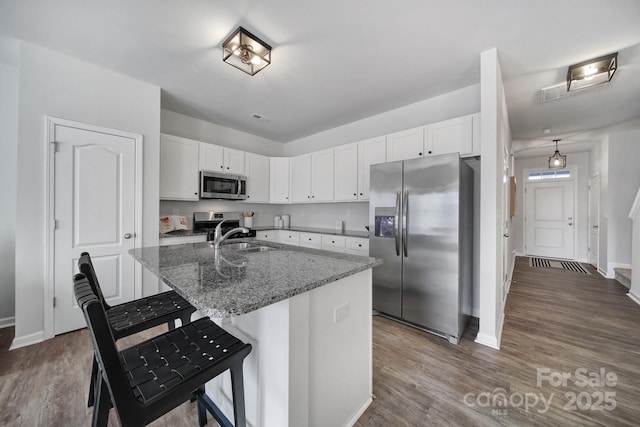 kitchen with white cabinets, light stone countertops, a center island with sink, and stainless steel appliances