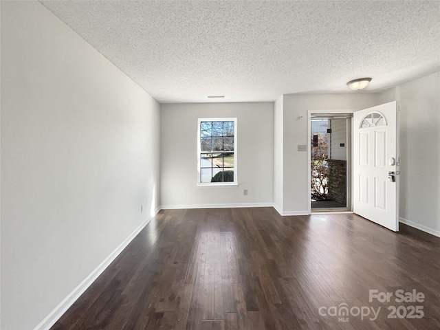 unfurnished room with baseboards, a textured ceiling, and dark wood-style floors