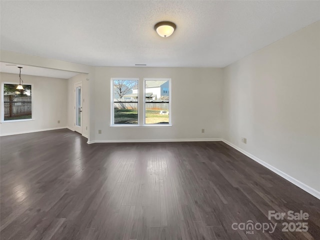 empty room with dark wood finished floors, a textured ceiling, and baseboards