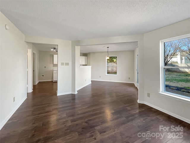 unfurnished living room featuring baseboards, dark wood-style flooring, and a textured ceiling