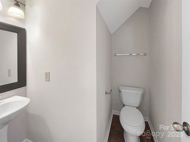 half bathroom featuring baseboards, toilet, and lofted ceiling