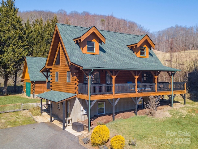 log-style house featuring a front lawn, fence, log exterior, roof with shingles, and driveway