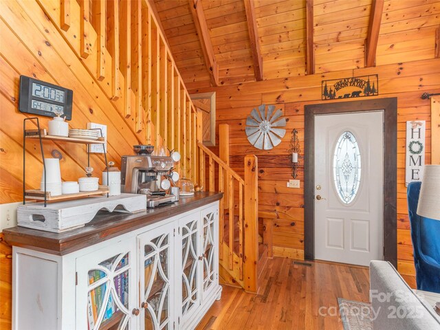 foyer featuring light wood-style floors, lofted ceiling with beams, wood ceiling, wood walls, and stairs