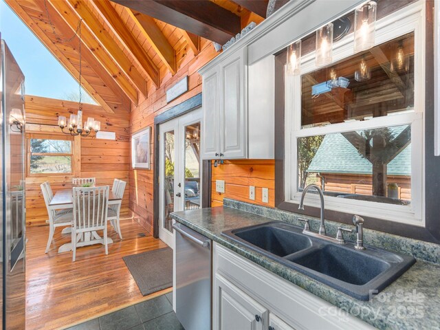 kitchen with a sink, french doors, white cabinetry, stainless steel dishwasher, and vaulted ceiling with beams