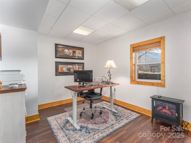 office area with a wood stove, dark wood-style floors, baseboards, and a paneled ceiling