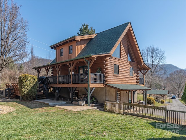 back of house featuring a deck with mountain view, board and batten siding, a patio area, log exterior, and a yard