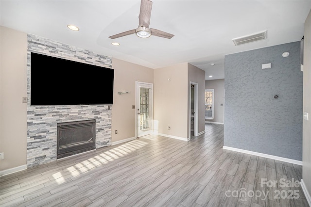 unfurnished living room with visible vents, wood finished floors, a fireplace, baseboards, and ceiling fan