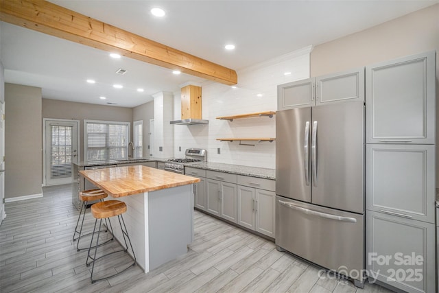 kitchen featuring wall chimney exhaust hood, gray cabinets, appliances with stainless steel finishes, and wood counters