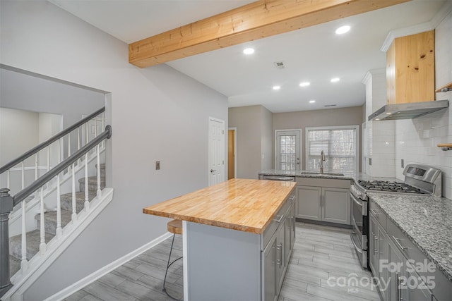 kitchen with a breakfast bar, a sink, gray cabinetry, stainless steel gas range oven, and butcher block counters