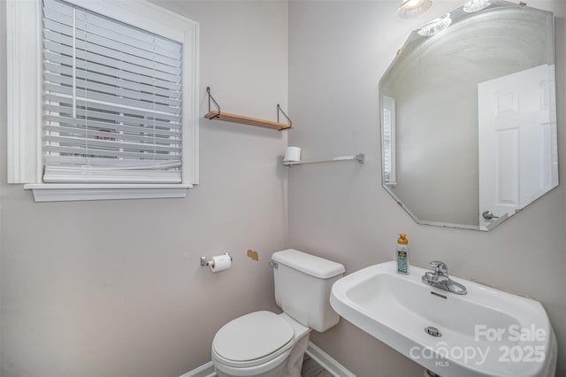 half bath with plenty of natural light, toilet, baseboards, and a sink