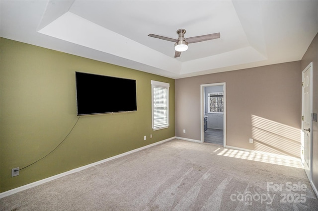 carpeted empty room featuring baseboards, a tray ceiling, and a ceiling fan