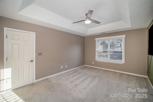 spare room with visible vents, a raised ceiling, a ceiling fan, carpet flooring, and baseboards