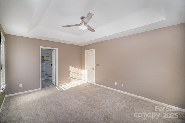 unfurnished bedroom featuring a tray ceiling, multiple windows, carpet flooring, and baseboards