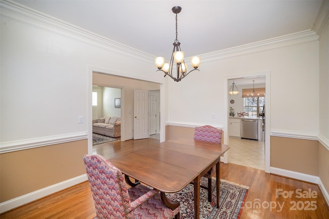 dining area with crown molding, baseboards, light wood-type flooring, and a notable chandelier