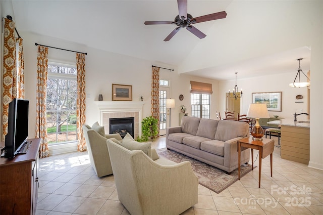 living area with high vaulted ceiling, light tile patterned floors, ceiling fan with notable chandelier, and a tile fireplace