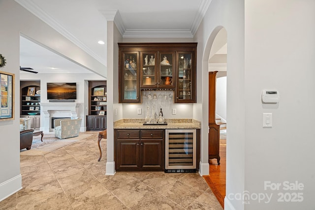 bar featuring beverage cooler, ornamental molding, built in features, a bar, and a fireplace