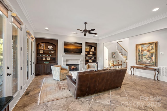 living area with ornamental molding, built in shelves, visible vents, and a lit fireplace