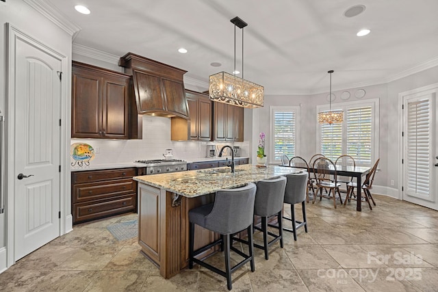 kitchen featuring decorative backsplash, crown molding, a kitchen island with sink, and a sink