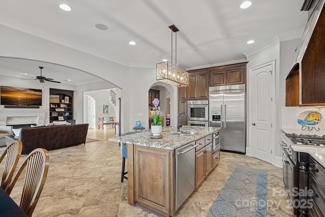 kitchen with arched walkways, a fireplace, light stone countertops, high end appliances, and ceiling fan