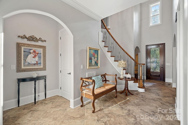 foyer featuring crown molding, stairway, baseboards, and arched walkways