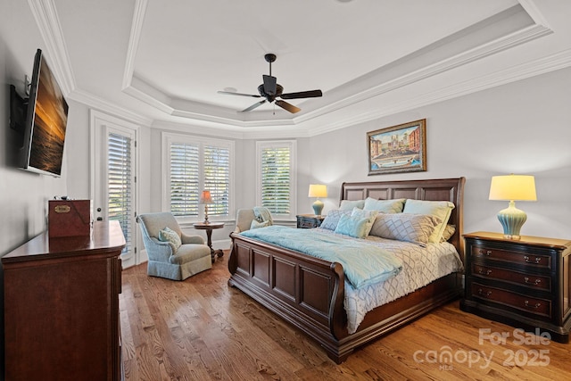 bedroom with ornamental molding, a raised ceiling, ceiling fan, and wood finished floors