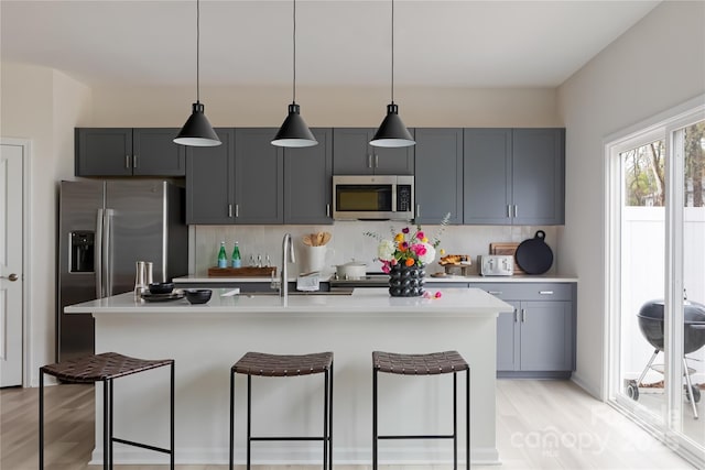 kitchen with a sink, stainless steel appliances, light countertops, a kitchen bar, and backsplash