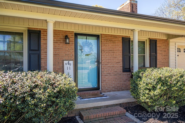 doorway to property featuring brick siding, covered porch, and a chimney