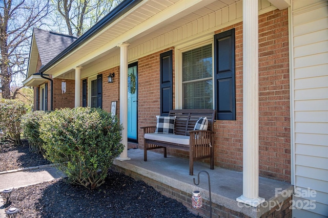 entrance to property featuring a porch, brick siding, and a shingled roof