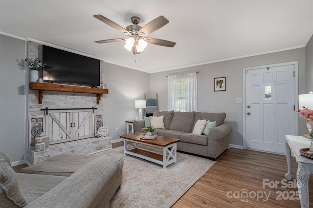 living room featuring ornamental molding, wood finished floors, a fireplace, baseboards, and ceiling fan