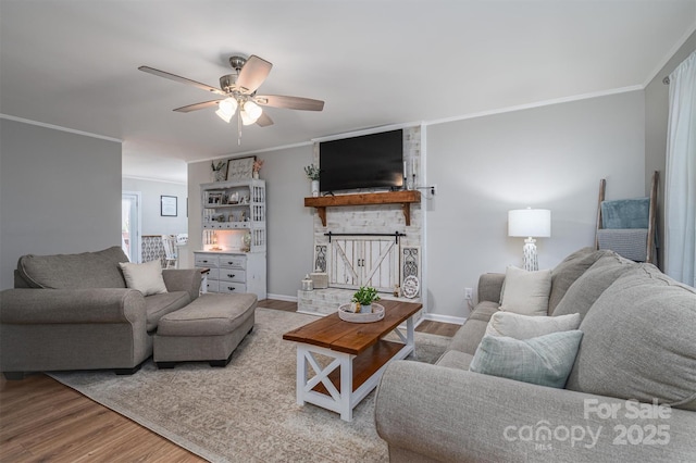 living area with a brick fireplace, wood finished floors, baseboards, and ornamental molding