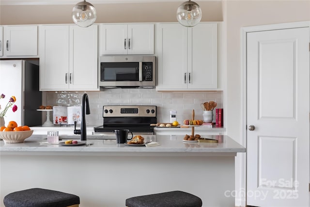 kitchen with a breakfast bar, backsplash, white cabinetry, and stainless steel appliances