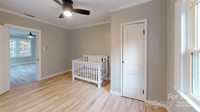 bedroom with visible vents, wood finished floors, a nursery area, crown molding, and baseboards