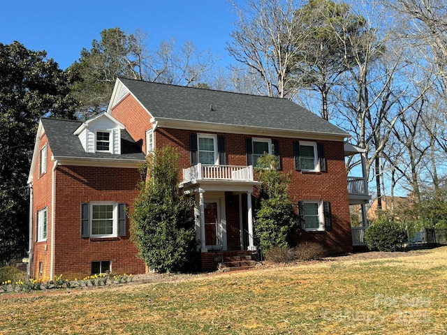 colonial inspired home with brick siding, a balcony, a front yard, and a shingled roof