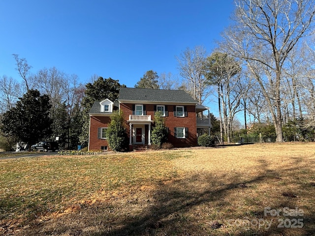 view of front facade with a front lawn, brick siding, and a balcony