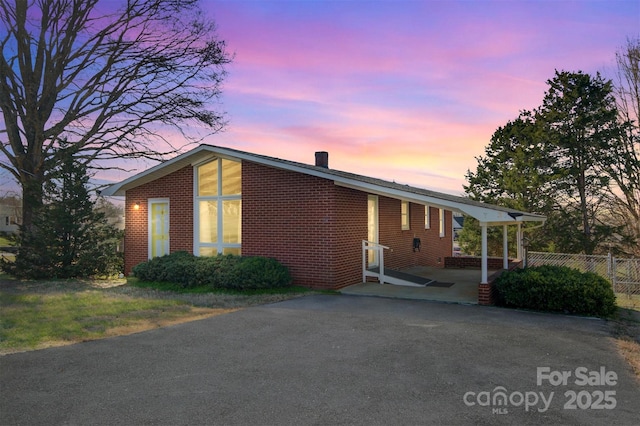 view of front of house featuring fence, driveway, a chimney, a carport, and brick siding