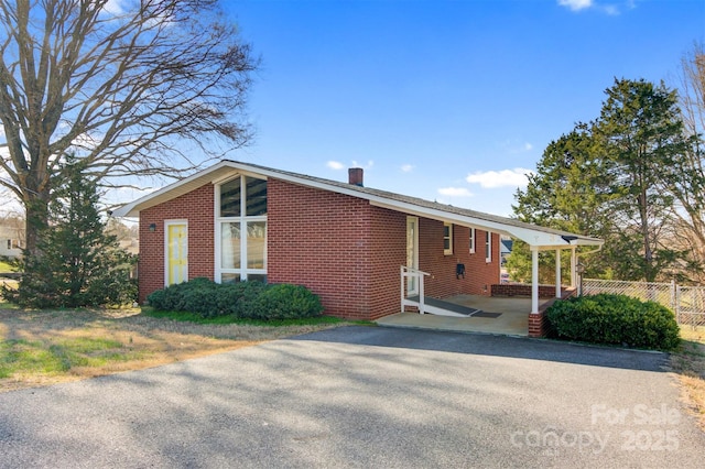 view of front of home featuring brick siding, an attached carport, fence, a chimney, and driveway