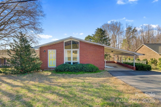 mid-century inspired home featuring an attached carport, a front yard, brick siding, and driveway