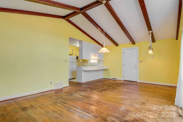 unfurnished living room with light wood-type flooring, visible vents, baseboards, and vaulted ceiling with beams