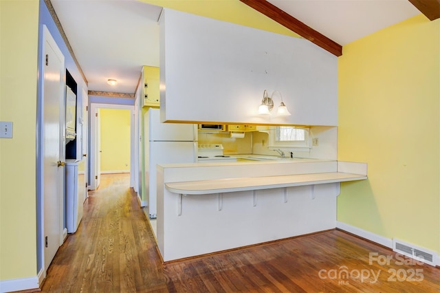 kitchen featuring visible vents, baseboards, beamed ceiling, wood finished floors, and white appliances