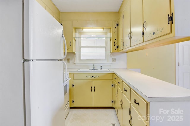 kitchen featuring light countertops, a peninsula, cream cabinets, freestanding refrigerator, and a sink