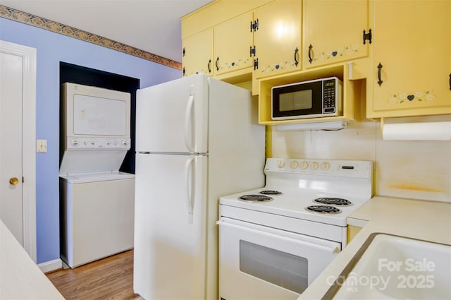 kitchen with light wood finished floors, light countertops, stacked washer and clothes dryer, cream cabinets, and white appliances