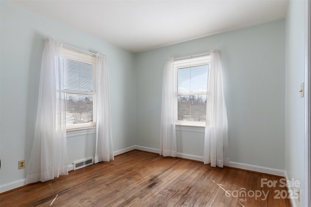 spare room with hardwood / wood-style floors, a healthy amount of sunlight, visible vents, and baseboards